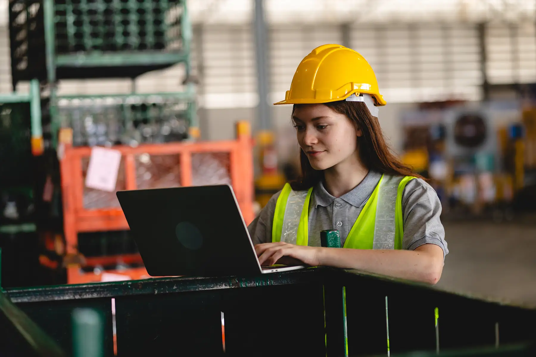 Engineer wearing a safety vest and hard hat working on a laptop in a research facility, representing R&D efforts using compact hydrogen storage systems for testing fuel cells and advanced energy technologies.